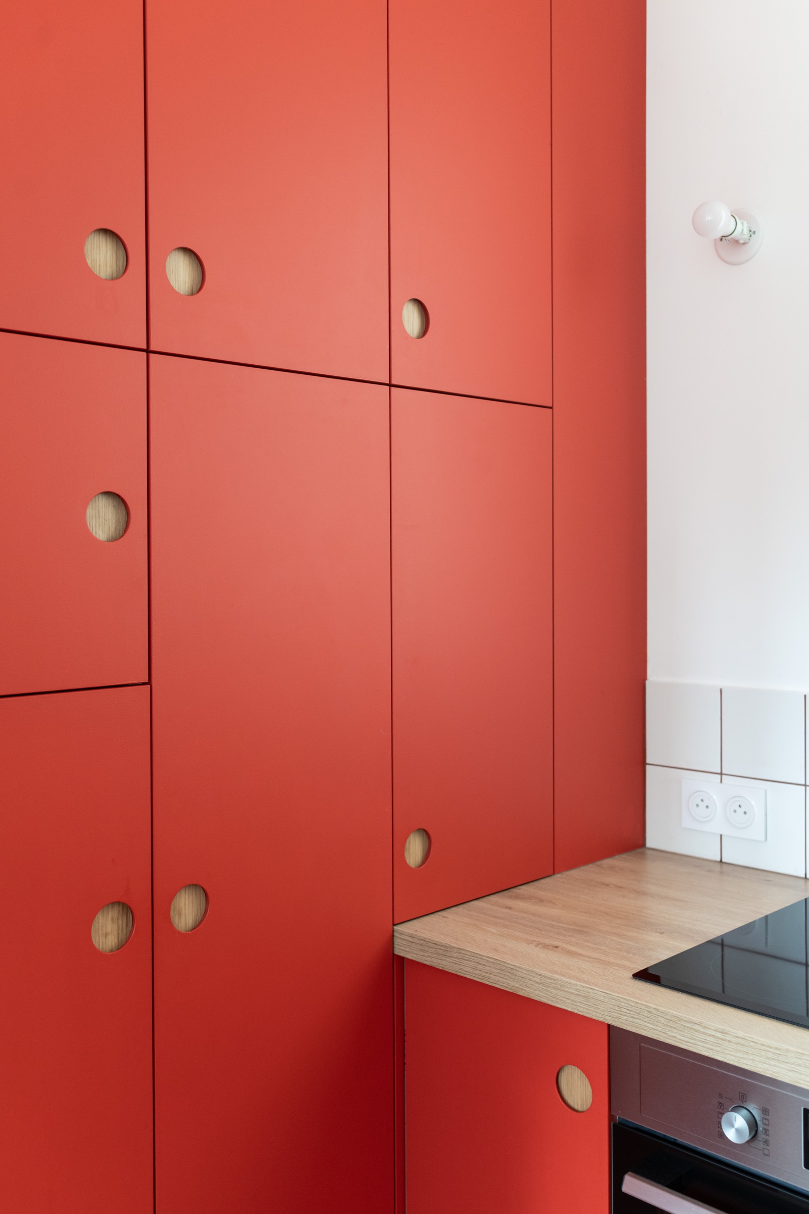 Placards rouges sur mesure avec poignées rondes encastrées laissant apparaître le bois