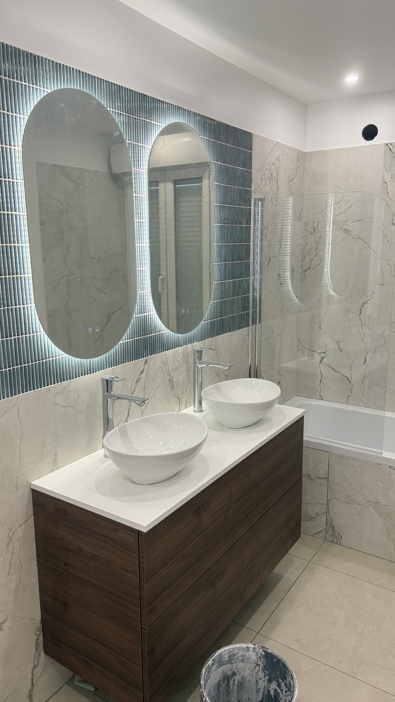 Salle de bains avec double vasque blanche, grand meuble sombre et miroir lumineux