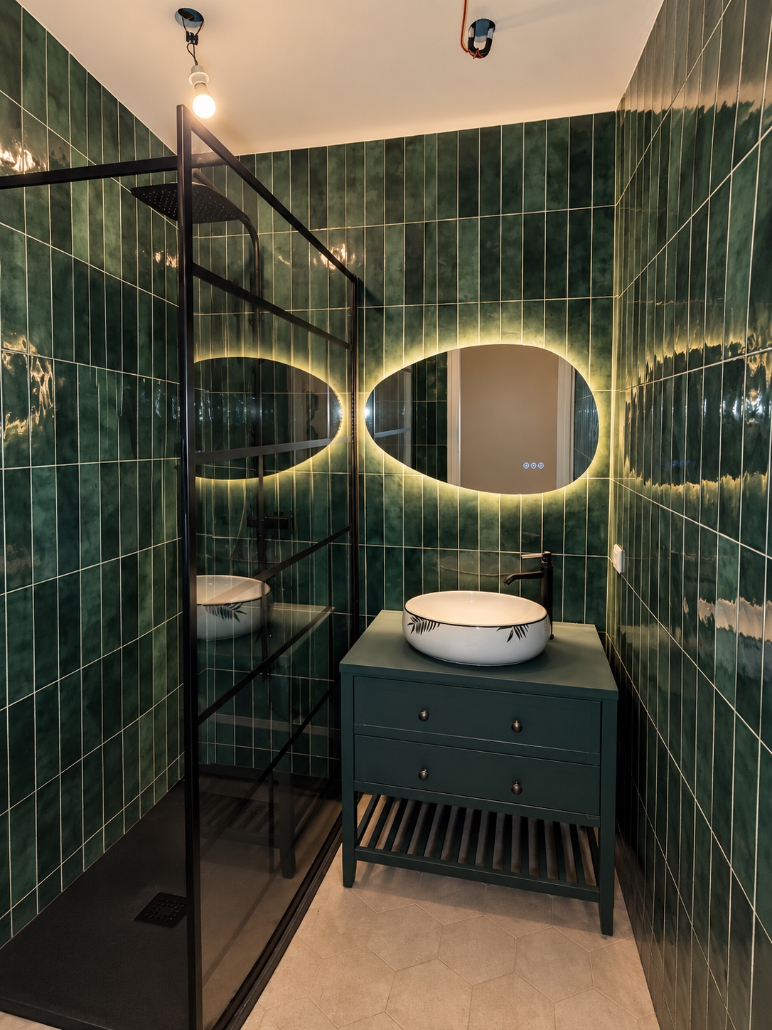 Salle de bains au carrelage vert avec deux miroirs lumineux et paroi noire